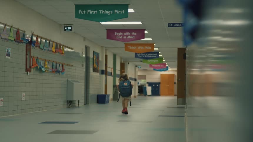 A child walks alone down a school hallway with a backpack
