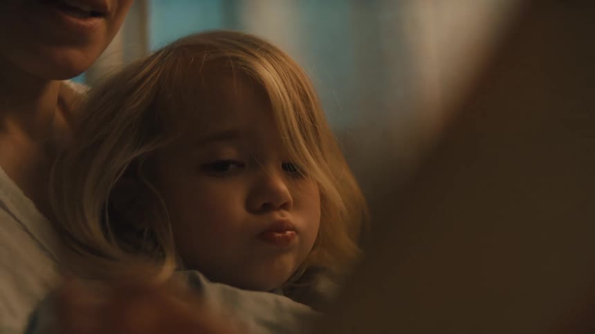A young blonde child cuddles closely with an adult watching something off screen with focused attention in warm lighting