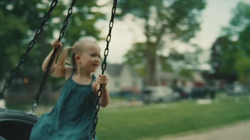 A woman gently pushing a smiling child on a tire swing in a park