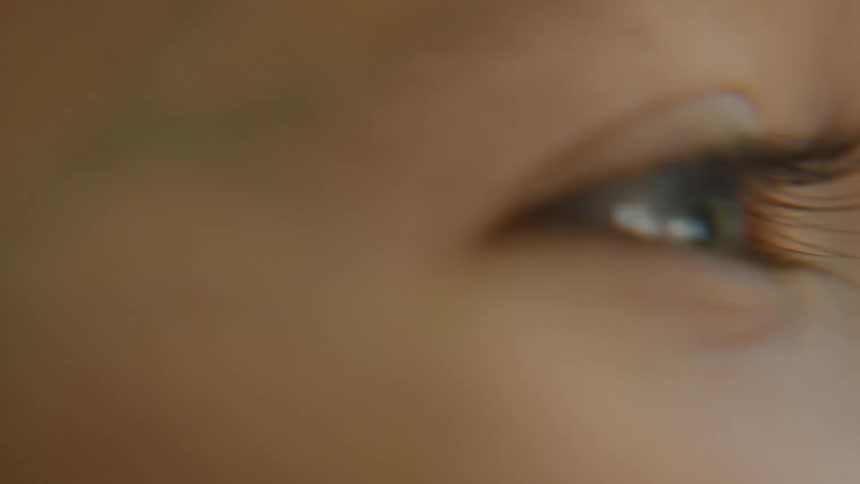 The video shows an extreme closeup of a persons eye which is bright blue and framed by long dark eyelashes the camera is out of focus at the start and then becomes sharp before going out of focus again