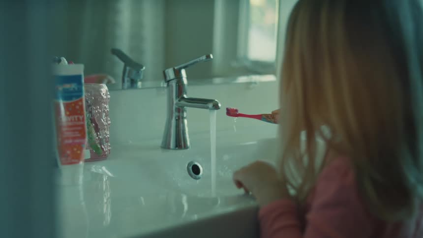 A young girl brushes her teeth at the bathroom sink at midday