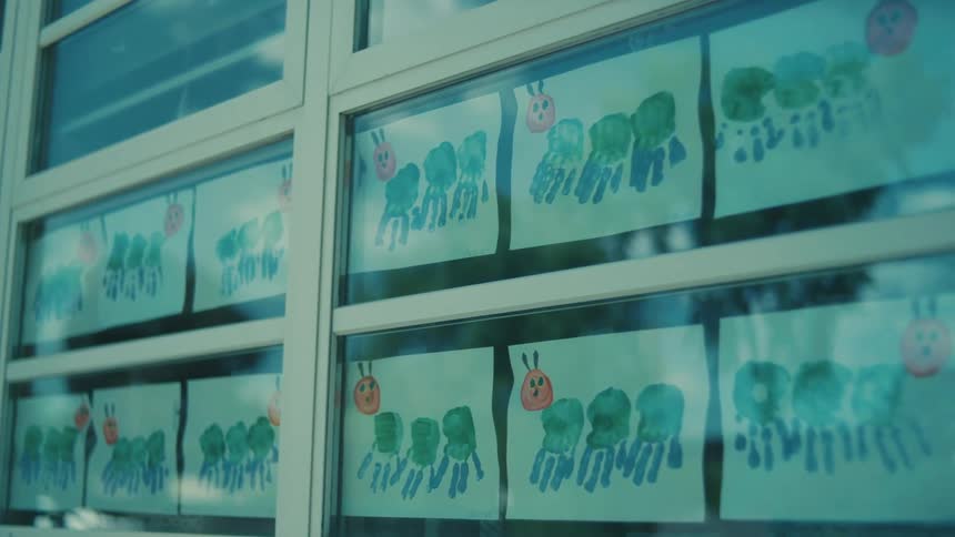 Child like paintings of caterpillars line the reflective windows on a large building during the day