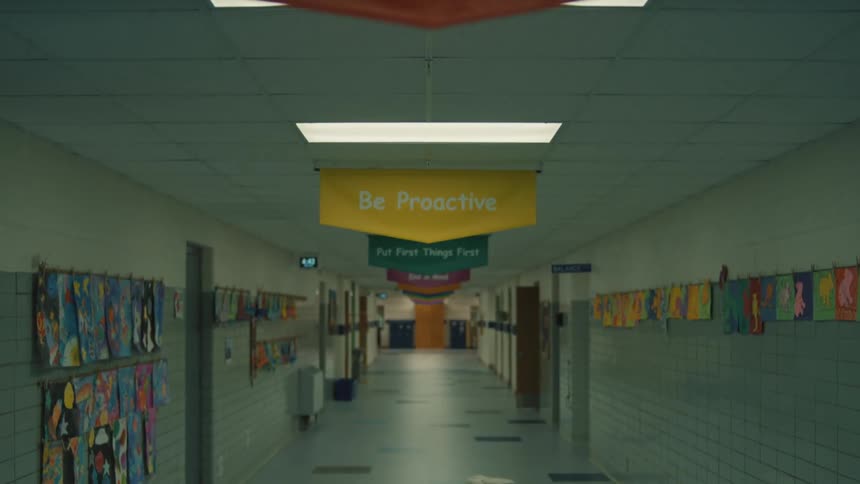 An empty school hallway decorated with motivational banners and student art then a boy and a girl enter the hallway