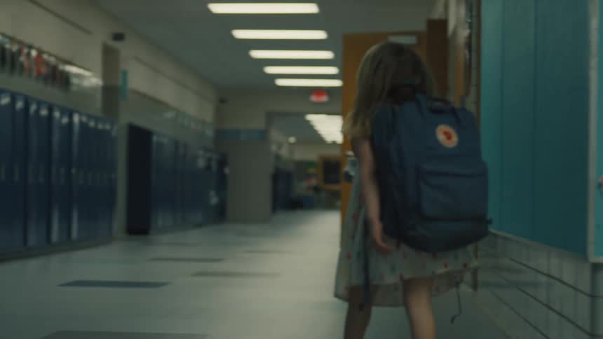 A little girl wearing a dress with a backpack is running down a school hallway she runs past colorful artwork on the walls and blue lockers before she turns around
