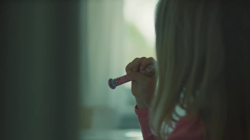 A closeup of a young girl with blonde hair brushing her teeth in a bathroom