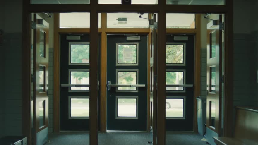 A set of large school doors one of which swings shut and closes