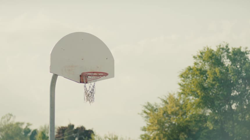 A basketball hoop with a torn net in a park