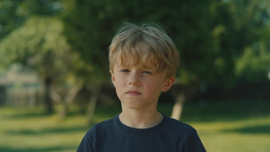A young boy standing in a clearing in a tree park looking sad