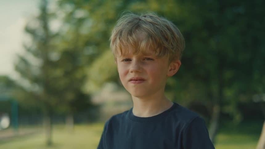 A young boy stands outside in a park on a sunny day