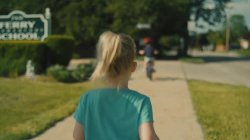 A mother and two children are walking down a sidewalk one child is running ahead while another rides a bicycle