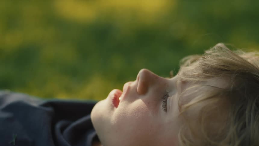 The video shows a person lying on their back on a grassy field looking up at the sky they are wearing a dark sweatshirt with the hood up the video is a closeup shot and only the persons face is visible