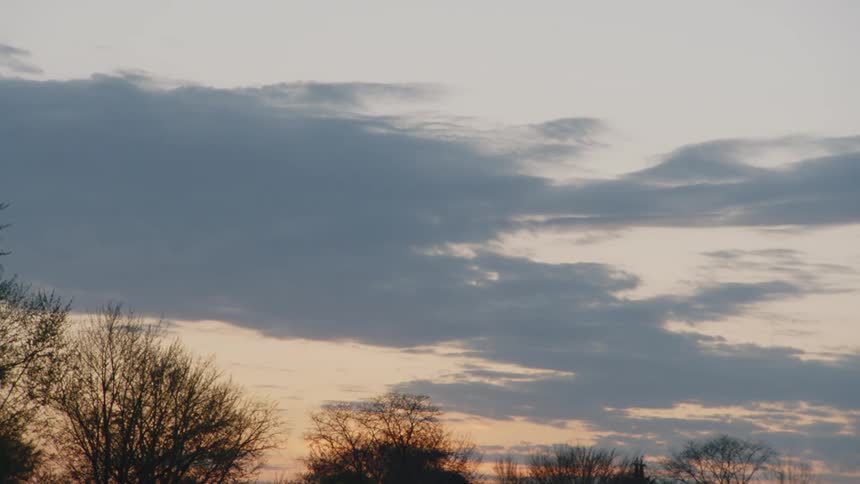The sky is filled with soft grey clouds at dusk with the silhouettes of trees visible against the horizon