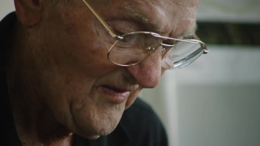 The video shows an intimate closeup of an elderly mans face with a soft focus on his wrinkled skin and the goldrimmed glasses resting on his nose the camera pans down slightly capturing the subtle movements of his mouth as he speaks