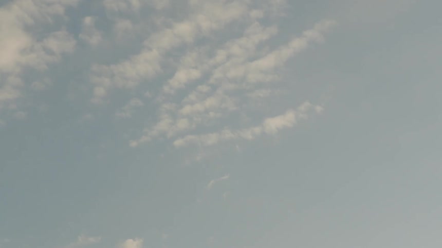 The video shows a timelapse shot of white fluffy clouds drifting across a hazy blue sky the movement of the clouds is steady and peaceful suggesting a calm day