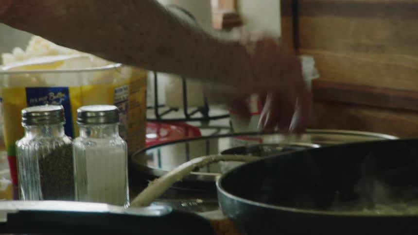 Elderly hand holds the lid of a pot in a home kitchen