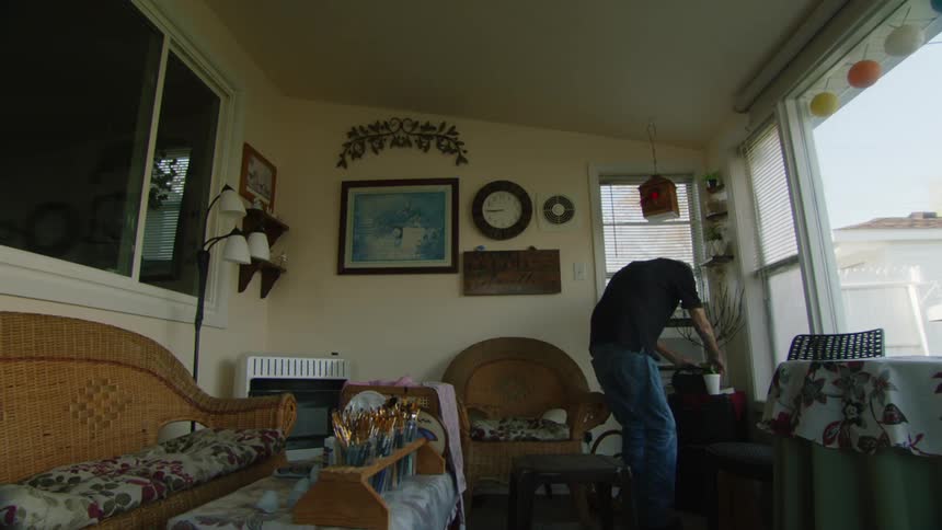 An elderly man adjusts an item inside a cozy sunroom