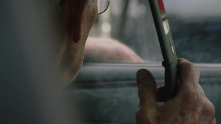 A man smokes a cigarette while holding a flip phone inside a car