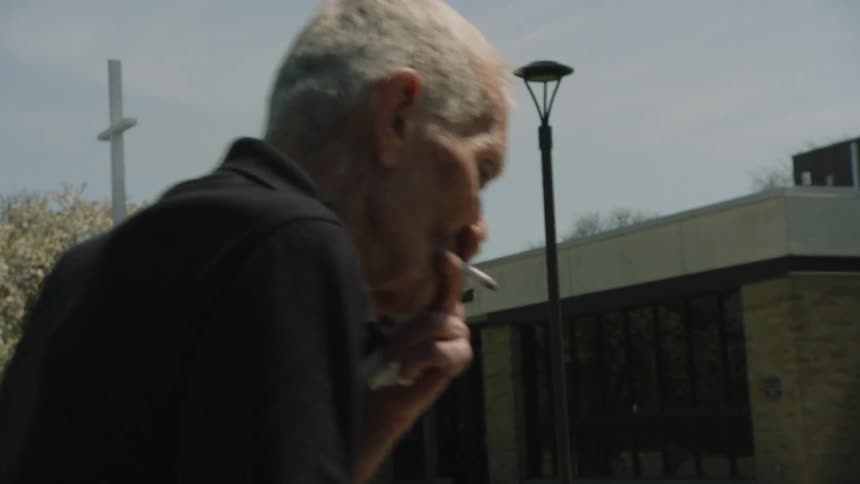 An elderly man smokes a cigar while walking toward a church