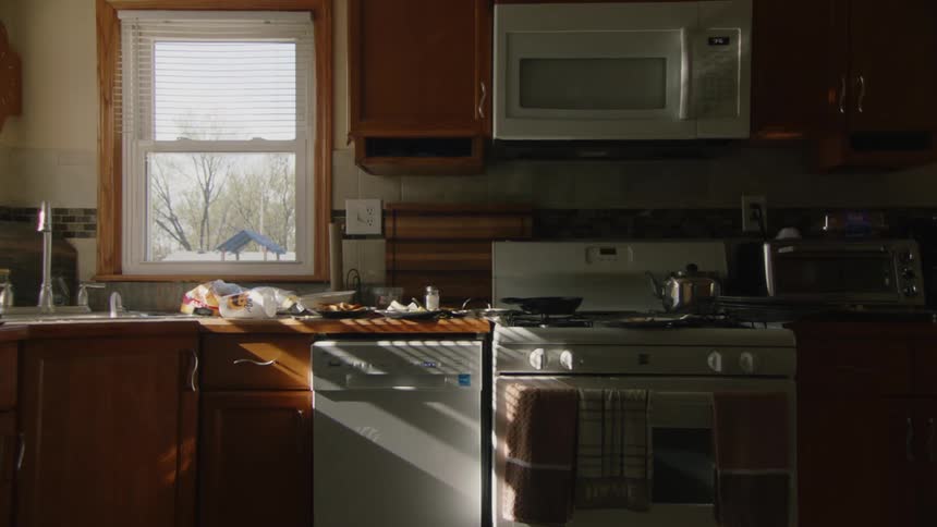 Kitchen lit by sunlight reveals sink stove and microwave
