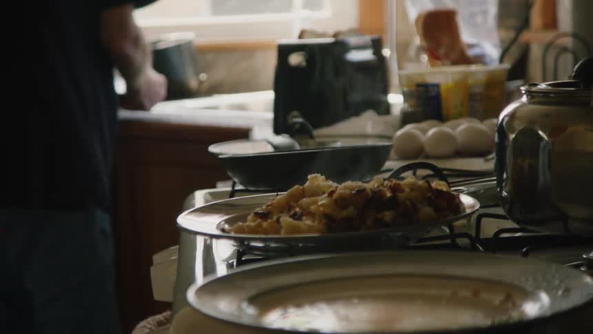 An elderly man is in a home kitchen preparing plates of food