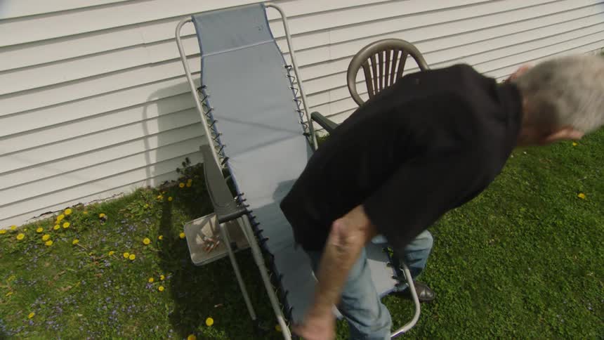 An elderly man relaxing and smoking a cigarette in a lounge chair in his backyard before he gets up to walk away