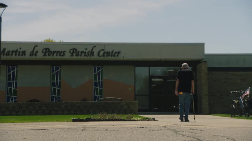 An elderly man walks with a cane toward a parish center