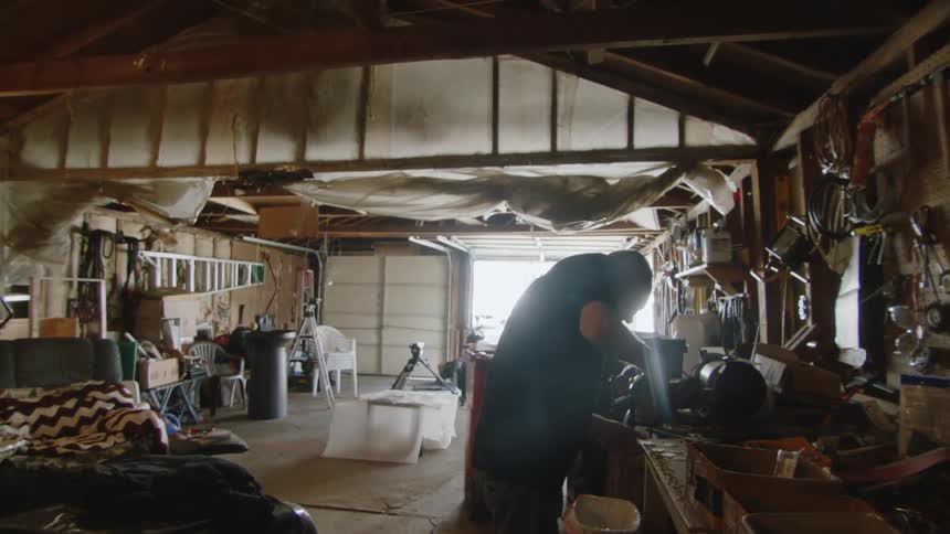A man working on a project in a messy garage workshop surrounded by various tools and equipment