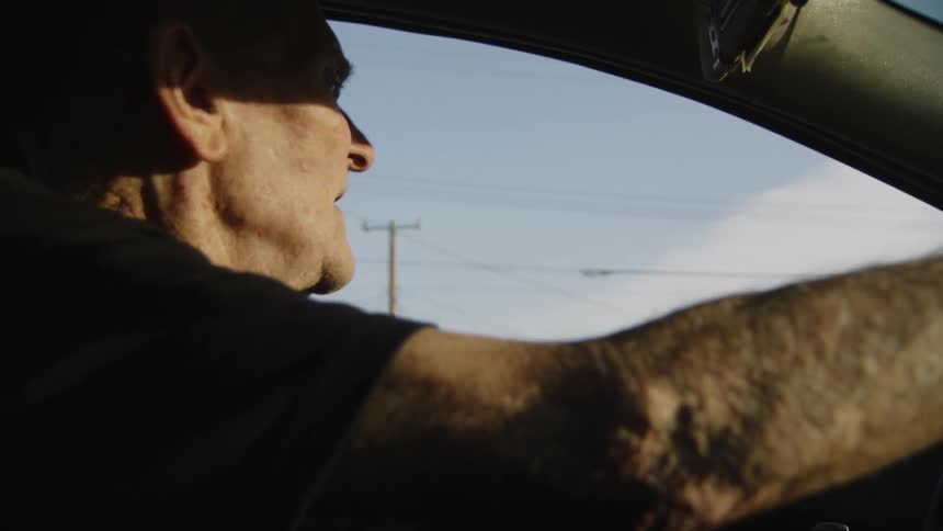 An elderly man driving a car glancing at the side of the road