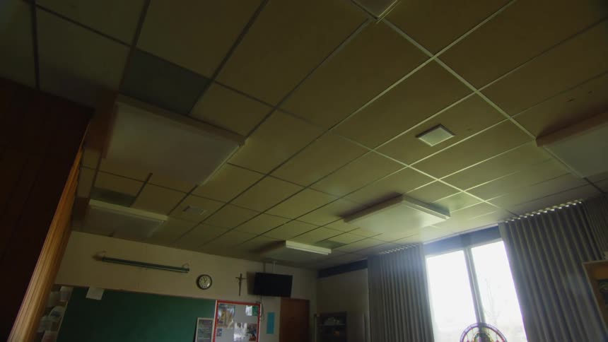Cross hangs on the wall next to a wall clock in a room with multiple round tables