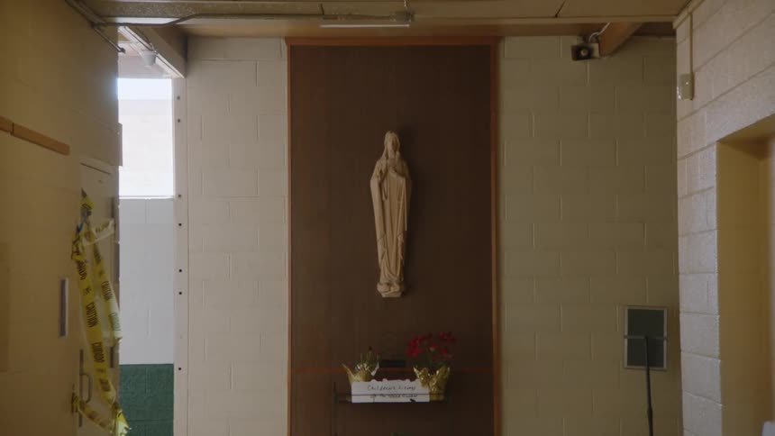The video shows a hallway with a statue of a saint at the end the camera slowly zooms in on the statue which is mounted on a brown wall with a small shelf underneath