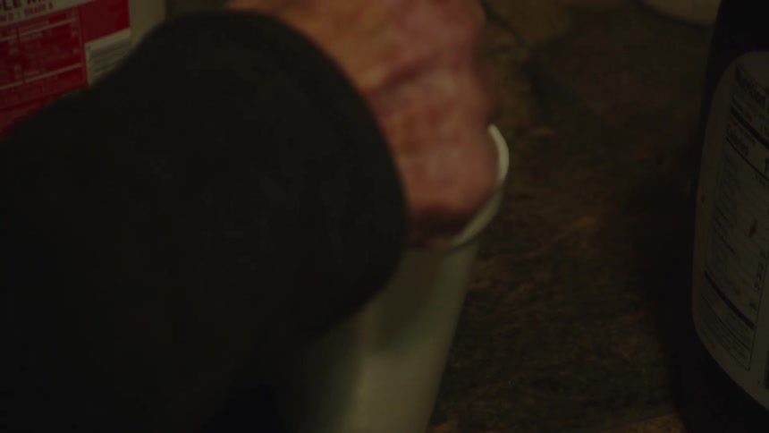 A persons arm wearing a black jacket stirs a cup of coffee in a plastic cup with a spoon