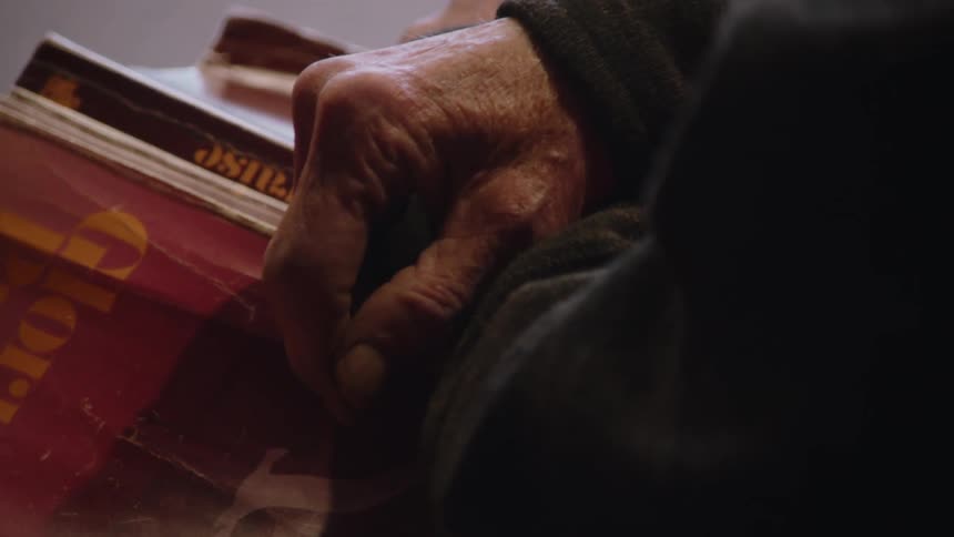 The video shows an elderly persons hands turning the pages of a book the books cover has a logo with the words glory and trust on it