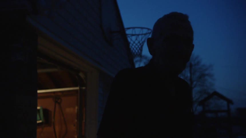 Elderly man smokes in silhouette outside at night