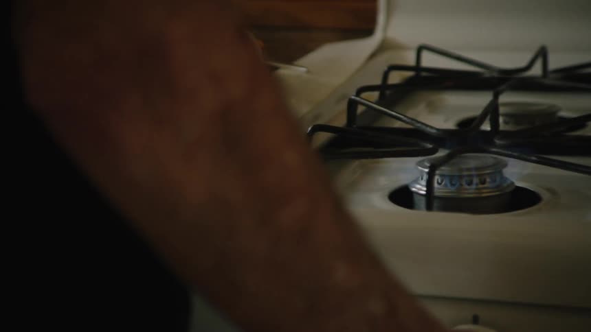 Elderly man turning on the stove and placing a frying pan on it