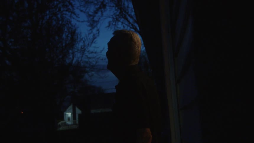 The video shows a person standing in a doorway at night silhouetted against a dark blue sky in the distance a lighted house is visible