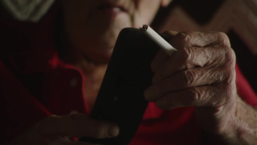 An elderly man is holding a cigarette and texting on his phone