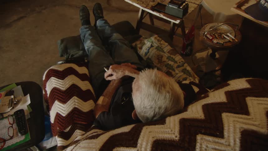 A man is sitting in a blanket covered chair smoking a cigarette
