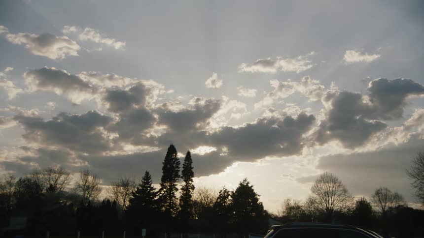 Falling sunlight on clouds over trees and a family car