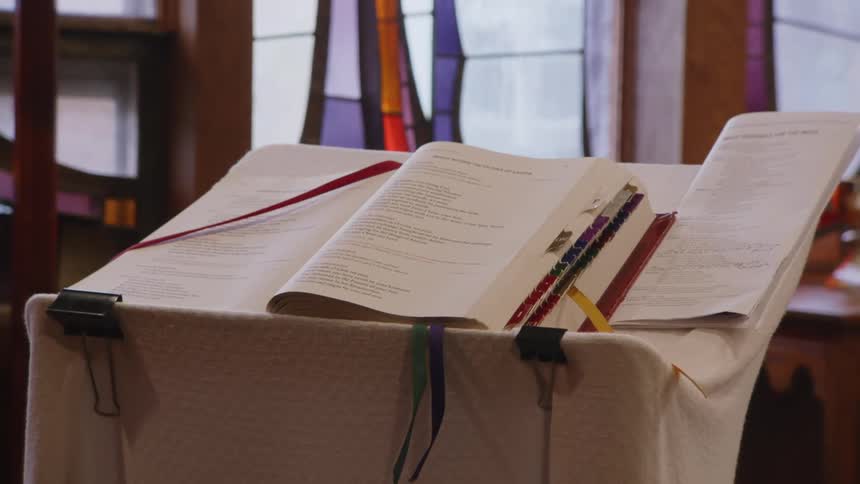 An open book rests on a lectern inside a church with stained glass windows