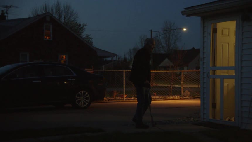 Elderly man walks toward the lit doorway of the house after getting out of the car