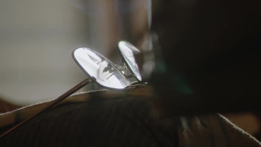 A closeup shot shows a pair of goldrimmed ovalshaped glasses with clear lenses the glasses are resting on a surface with light reflecting off the lenses and frames