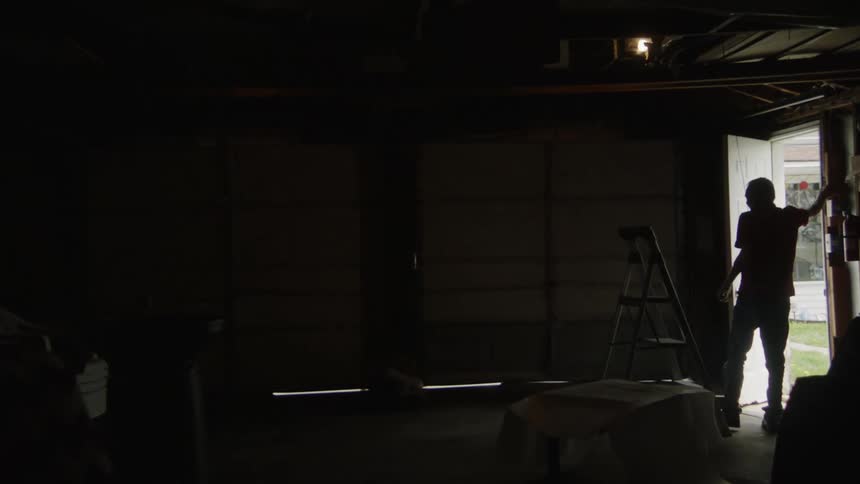 An elderly man is closing the door of a cluttered garage