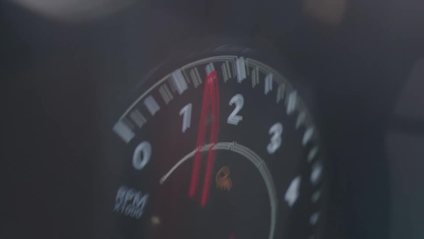 A shaky blurry view of a cars tachometer shows the red needle swinging on the instrument display