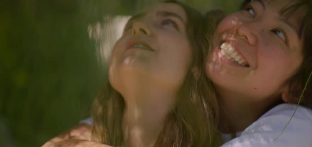 The video shows a closeup of two smiling women looking up and laughing together the shot is tightly framed focusing on their joyful expressions and the warmth of their interaction