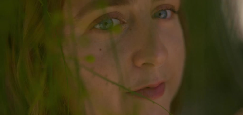 Young blonde woman among green leaves of a tree