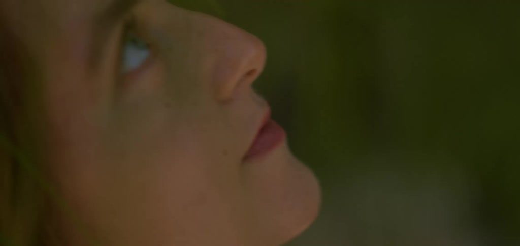The video shows an intimate closeup of a womans profile revealing her peaceful and thoughtful expression as she looks upwards sunlight filters through the foliage casting dappled light on her face and highlighting her features