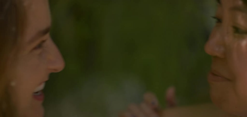 The video features a closeup shot of two womens faces seen in profile laughing and looking toward each other the camera captures their expressions of genuine joy and their smiles in a soft natural lighting
