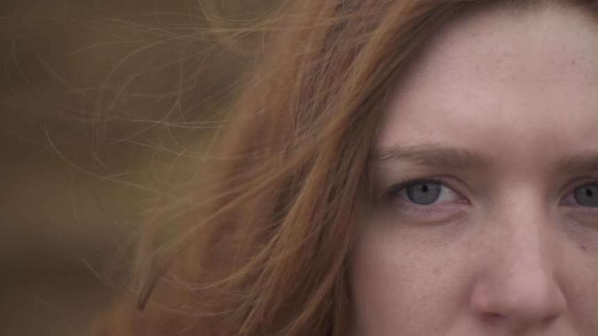 Close up of a woman with red hair and green eyes while a breeze blows her hair back