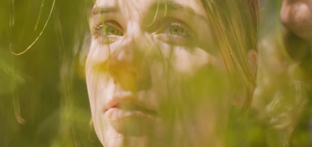 Young woman with light eyes among green leaves of a tree during the day