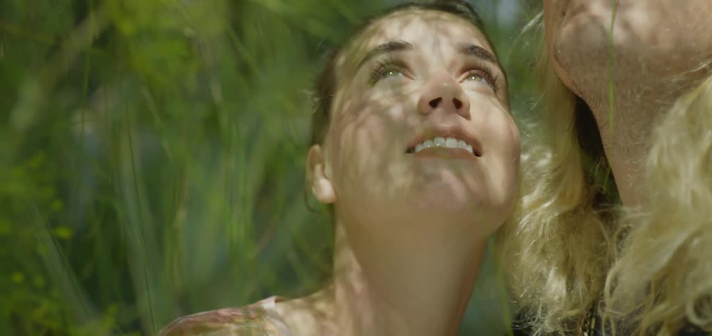 The video shows an intimate closeup of a womans face with her eyes closed and a peaceful expression the sunlight filters through the surrounding leaves casting soft moving shadows across her face and highlighting her features